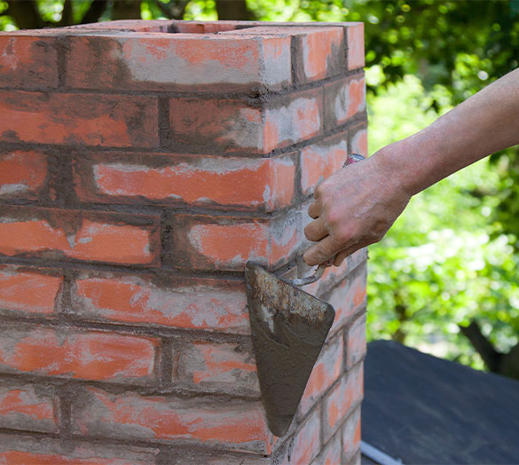 Mason applying mortar to a newly constructed red brick chimney with a trowel